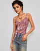 A woman modeling a mauve pink lace corset-style camisole top with ruffle details and tie-front keyhole, paired with blue jeans against a light gray studio background.