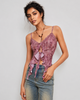 A woman modeling a mauve-purple lace camisole top with ruffle details and tie-front closures, paired with light-wash blue jeans against a light gray studio background.