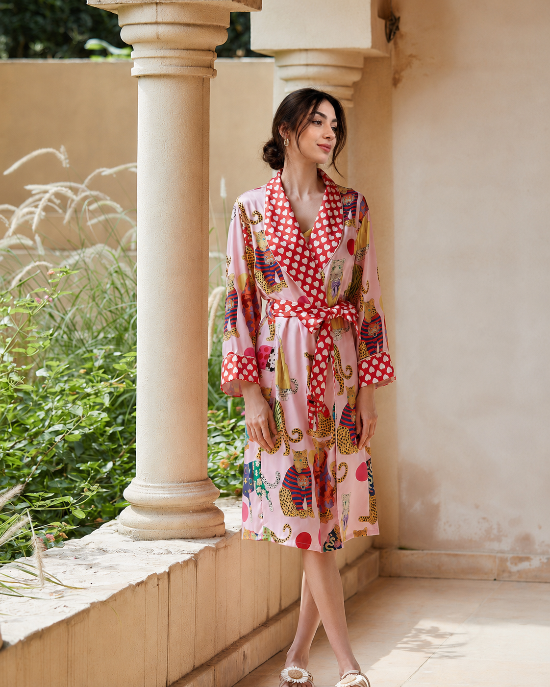 A woman wearing a pink and red patterned kimono robe with a red and white polka dot collar and waist tie, standing on a beige stone porch with columns.