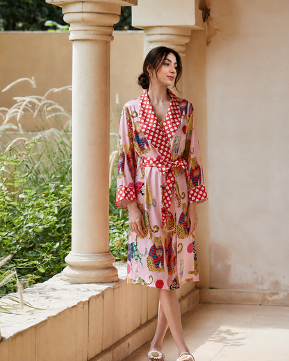 A woman wearing a pink and red patterned kimono robe with a red and white polka dot collar and waist tie, standing on a beige stone porch with columns.