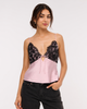 A woman modeling a color-block camisole top with a black lace upper section and a light pink satin lower section, paired with black jeans against a plain white studio background.