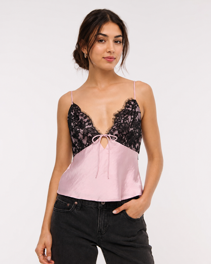 A woman modeling a color-block camisole top with a black lace upper section and a light pink satin lower section, paired with black jeans against a plain white studio background.