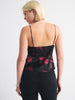 A woman shown from the back wearing a black spaghetti-strap camisole top with a red floral pattern and black jeans, against a plain light gray studio background.