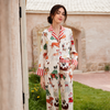A woman stands outdoors wearing a two-piece pajama set with a cream background and a colorful cartoon dog print, featuring red-and-white striped collar and cuffs. The setting includes a stone building, grass, and a doorway on the left.