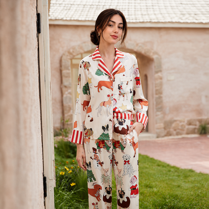 A woman stands outdoors wearing a two-piece pajama set with a cream background and a colorful cartoon dog print, featuring red-and-white striped collar and cuffs. The setting includes a stone building, grass, and a doorway on the left.