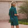 A woman stands outdoors wearing a matching short-sleeve button-front top and shorts set in dark teal green with thin white vertical stripes.