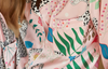 A close-up of a person wearing a light pink satin pajama shirt with a colorful botanical and animal print, featuring green leaves, blue flowers, and black-and-white leopard spots.