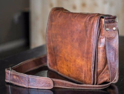 Compact leather men’s messenger bag in rich chestnut brown, styled with a watch and wallet on a wooden table.