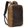 Canvas laptop backpack carried by hand, showing tan waxed canvas, dark brown contrast section, top handle, and shoulder straps.