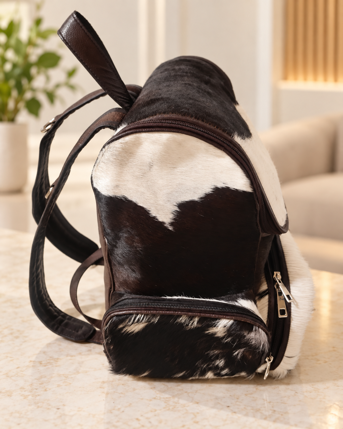 Cowhide mommy backpack opened to reveal brown lined interior storage beneath the large leather flap and zippered sections.
