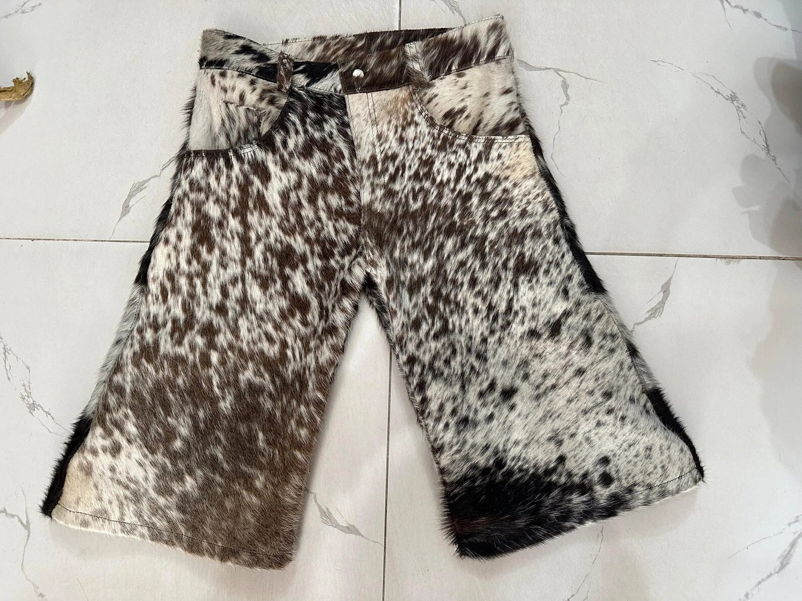Tricolor cow skin shorts featuring black, brown, and white patterns. Each pair is unique, made from hair-on leather with a western-style cut.
