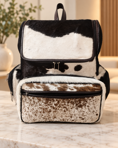 Cowhide mommy backpack in brown and white hair-on hide with flap top, leather trim, and front zip pocket.