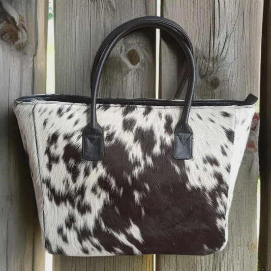 Genuine cowhide tote bag for women featuring black and white hair-on hide and sturdy leather straps. A bold western shoulder purse with natural texture.

