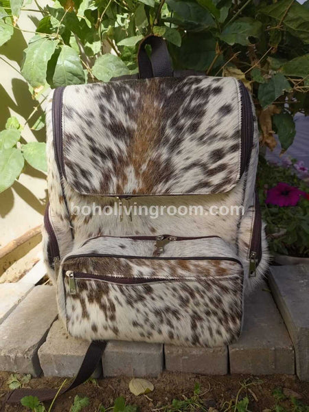 Brown and white cowhide backpack with leather straps and a front buckle closure.