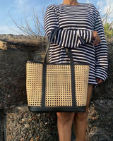 Stylish rattan beach bag with genuine leather accents, displayed against a tropical setting, emphasizing its versatility and fashion-forward design.