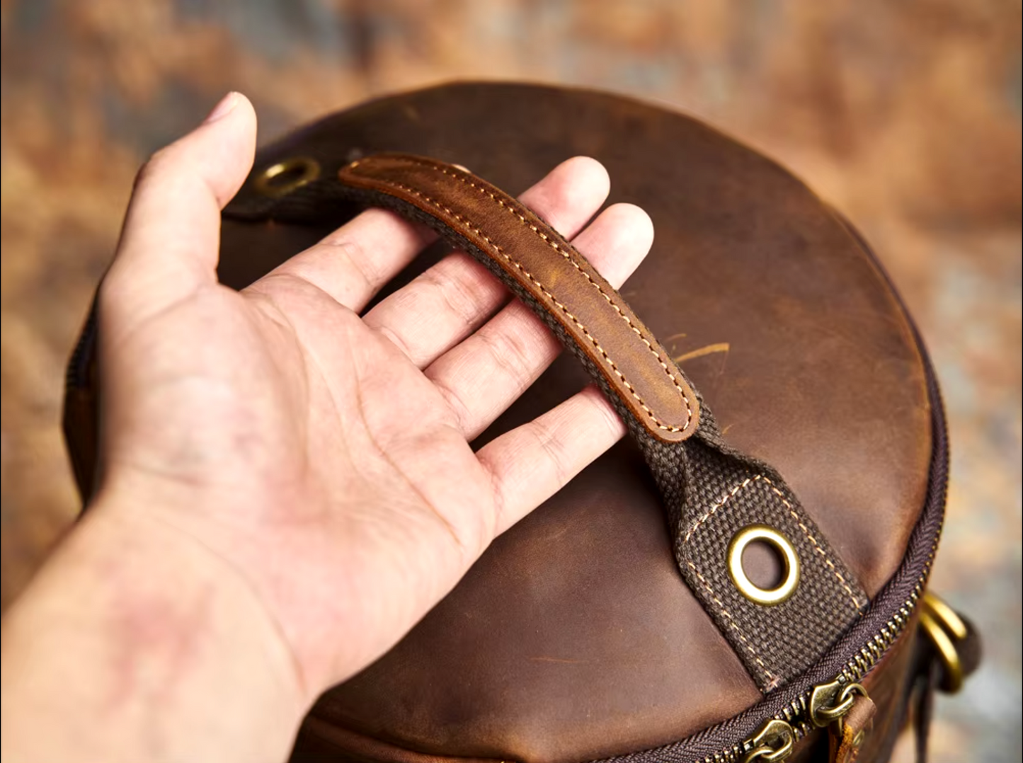 Classic leather backpack with a sleek design, adjustable straps, and front pocket detailing, displayed on a rustic surface.