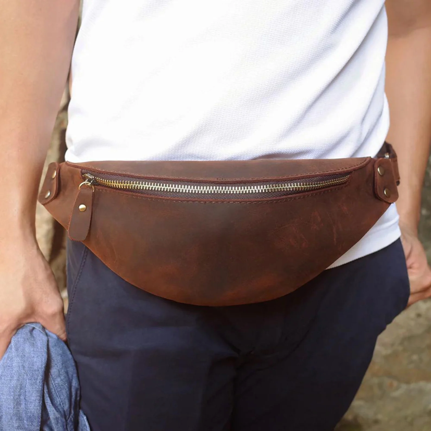 A sleek brown leather messenger bag with adjustable strap, resting on a rustic wooden table