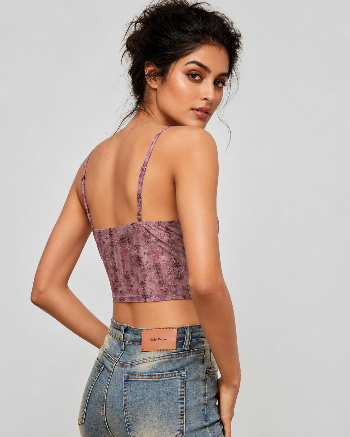 A woman shown from the back wearing a mauve-purple textured spaghetti-strap crop top and light-wash blue jeans against a light gray studio background.