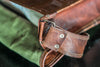 Stylish tan leather men’s messenger bag with a padded shoulder strap, hanging from the back of a chair.