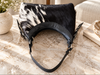 Cowhide purse styled for shoulder carry with hair-on cowhide, black trim, rounded shape, and dark strap.