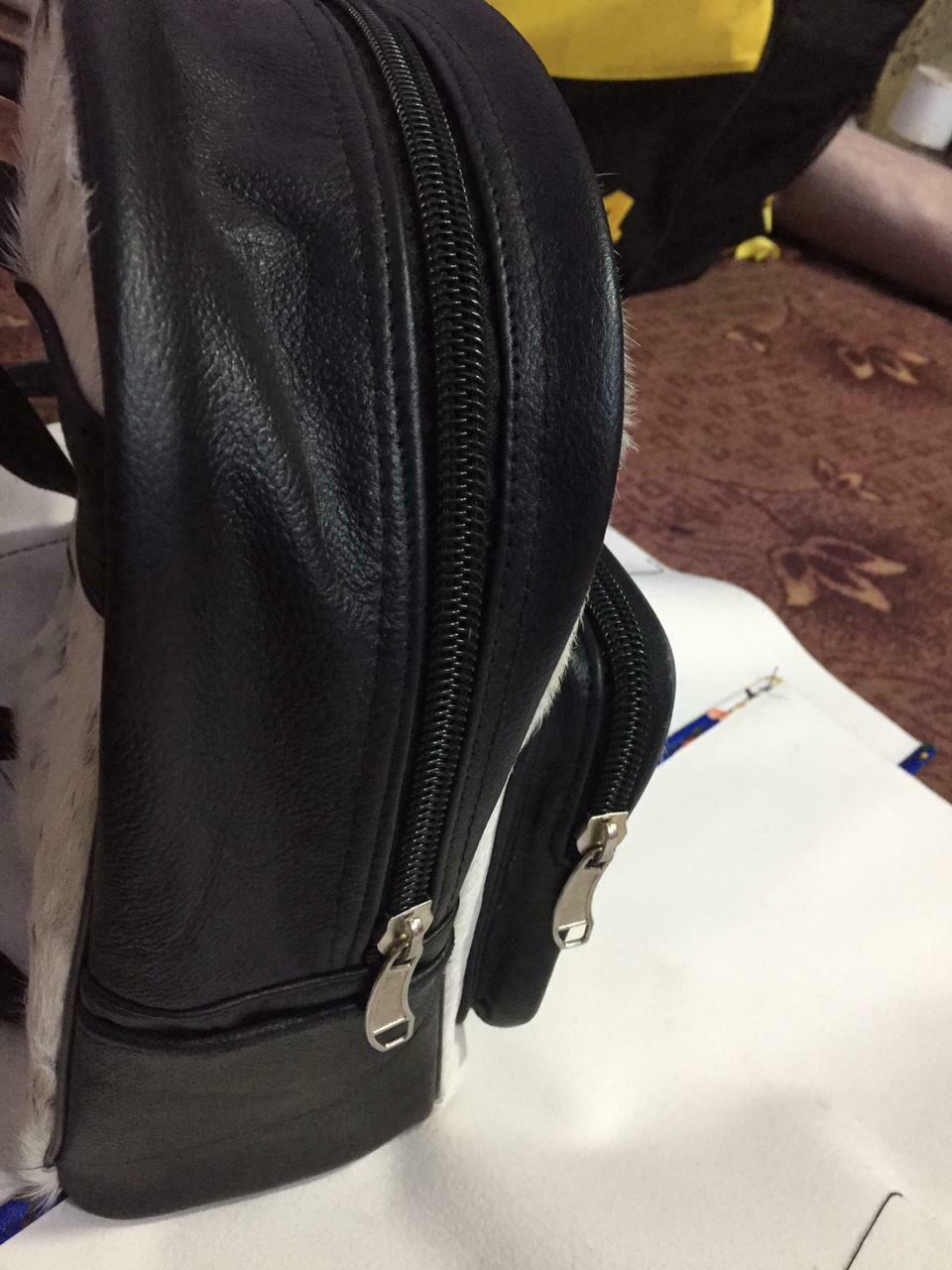 Cowhide backpack on a wooden table, surrounded by travel essentials like a camera, notebook, and sunglasses.