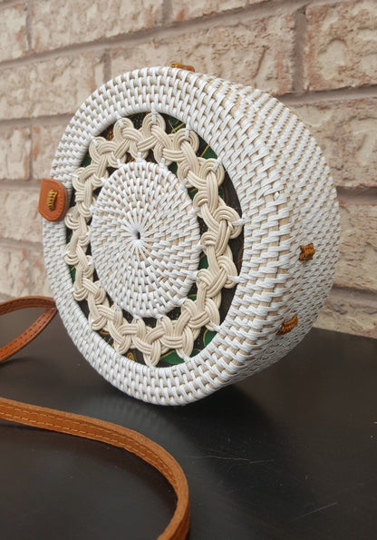 Stylish handcrafted rattan bag with natural texture, round shape, and detailed weaving, displayed outdoors.