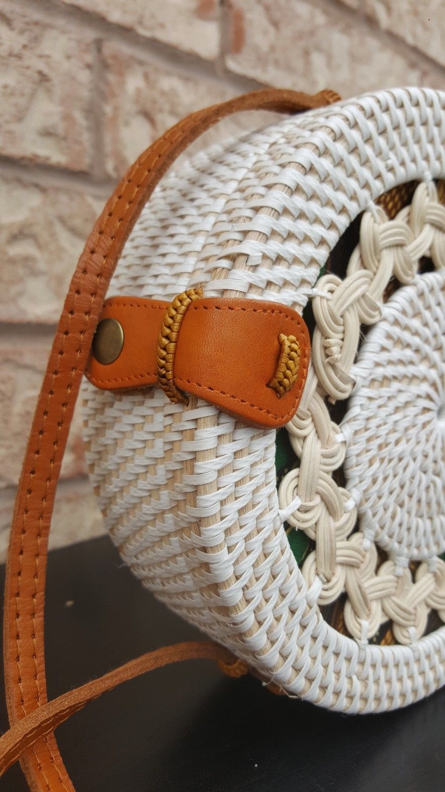 Chic rattan purse with a compact design, fine weaving details, and a leather buckle, displayed on a fabric surface.