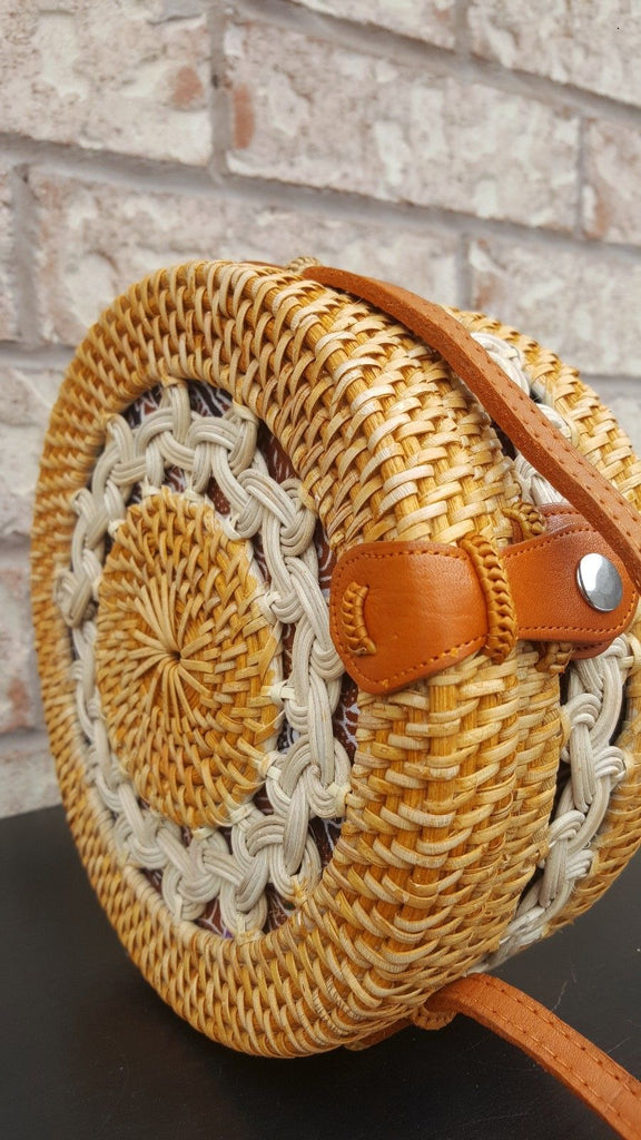 Round rattan bag with intricate woven design, resting on a wooden table, sunlight casting soft shadows.